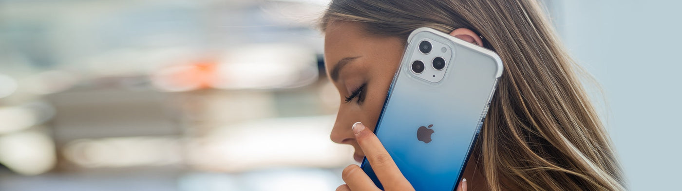 An Phone 12 Pro Max is covered with a blue gradient case from Raptic while a woman holds it to her ear for a phone call.